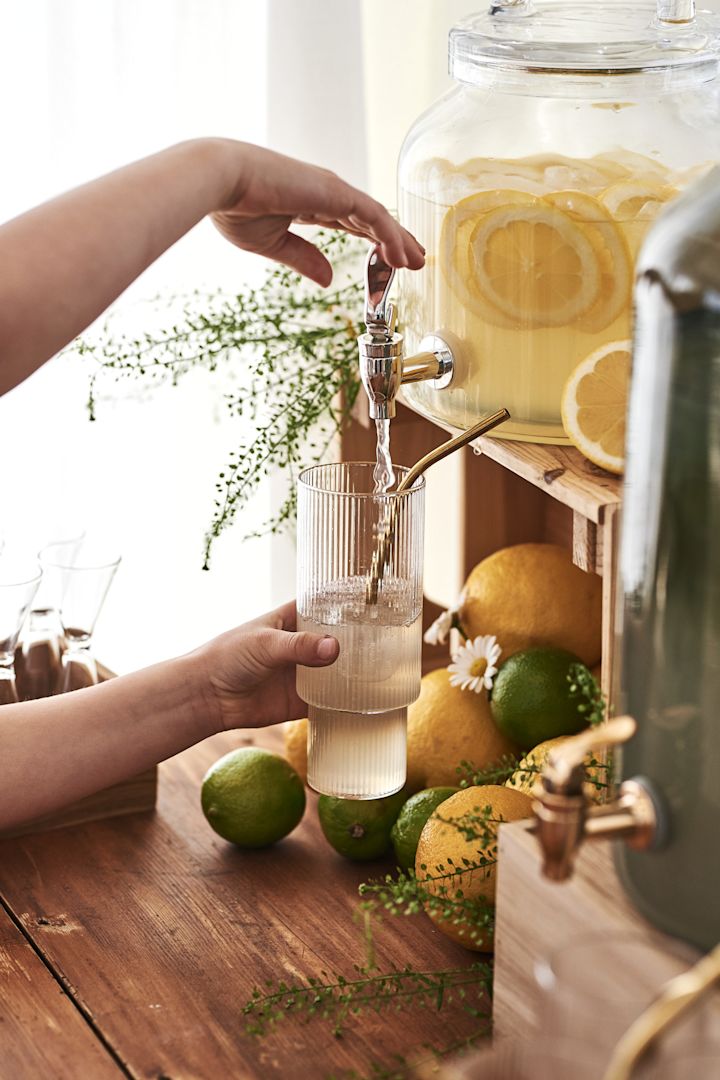 Try a simple cocktail recipe made with ginger and mint, here you see a hand pour the lemonade from the pitcher surrounded by lemon and limes. 